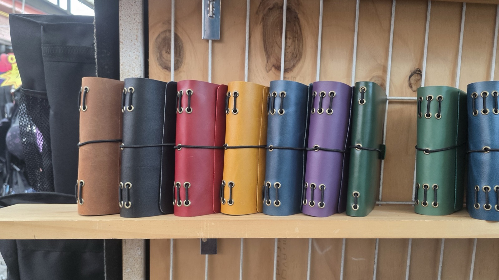 Fila de cuadernos artesanales de cuero en distintos colores sobre una repisa de madera.